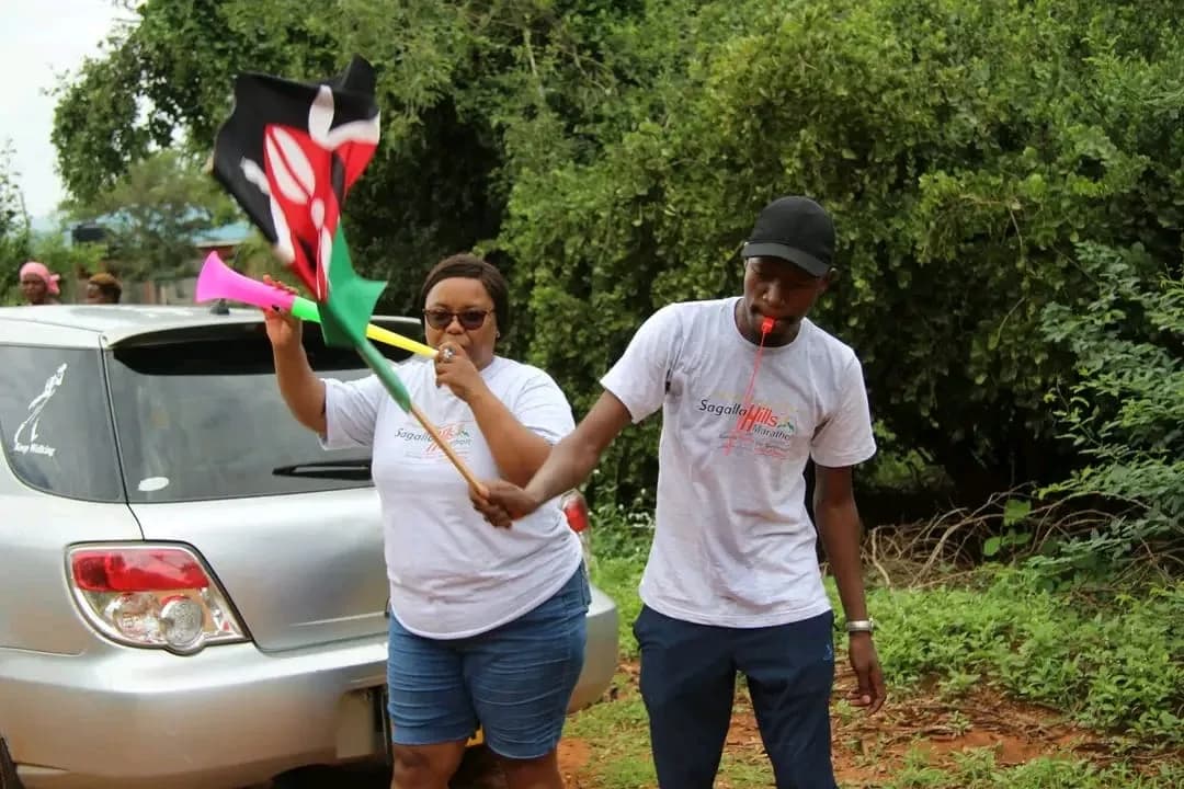 Two travellers waving a Kenyan flag beside a car